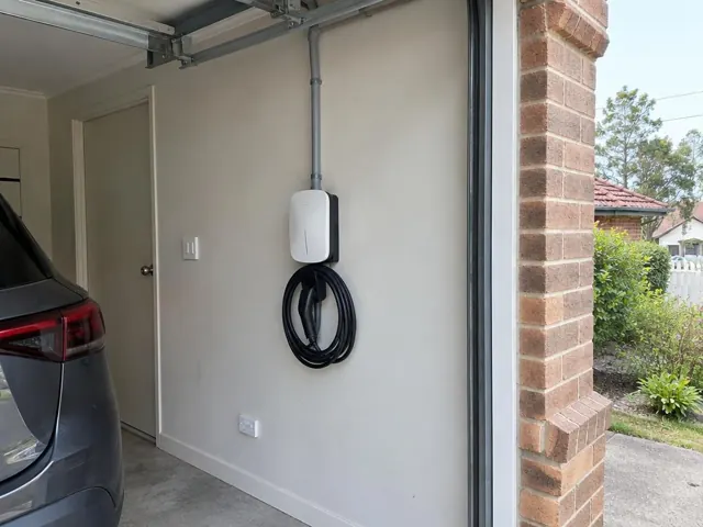 Wall-mounted EV charger with coiled cable in a garage beside a parked car in Adamstown