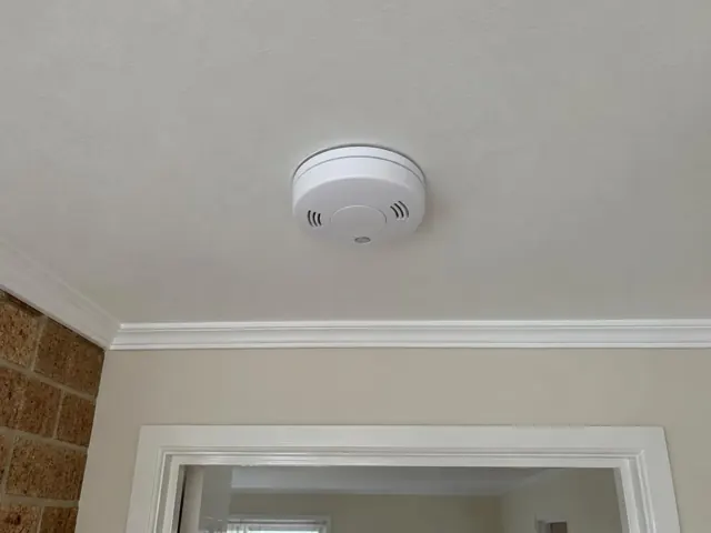 Ceiling-mounted smoke alarm above a doorway in a plaster-lined home interior in Adamstown Heights